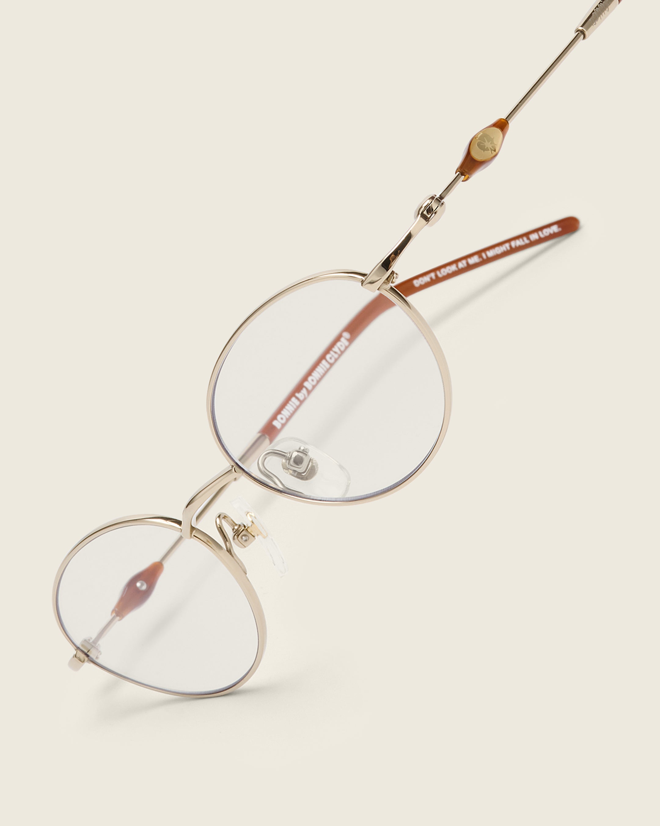 Slim, oval gold titanium frames with adjustable nose pads and lightweight acetate arm temple. Detail view.