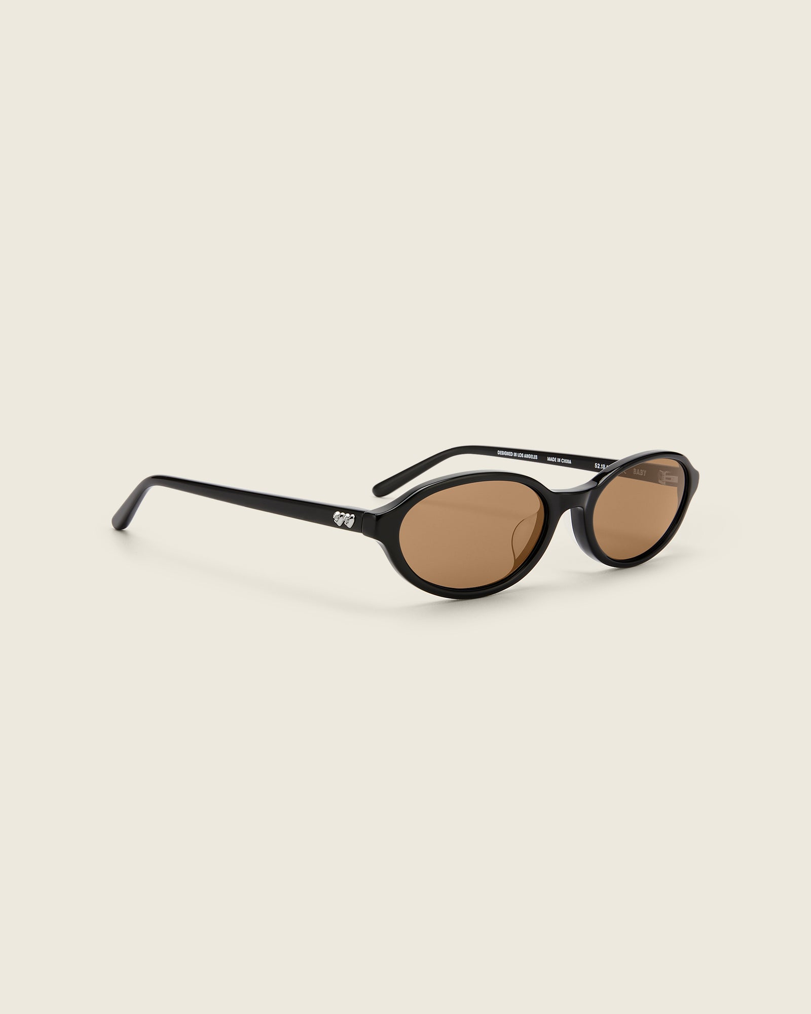 Bonnie Clyde Baby oval sunglasses in black acetate with brown lenses and double heart detailing on the arms, three-quarter view